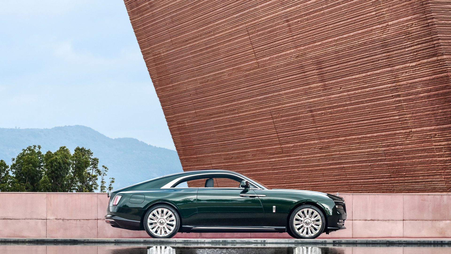 Side-profile shot of a green Rolls-Royce Spectre near a unique shaped structure