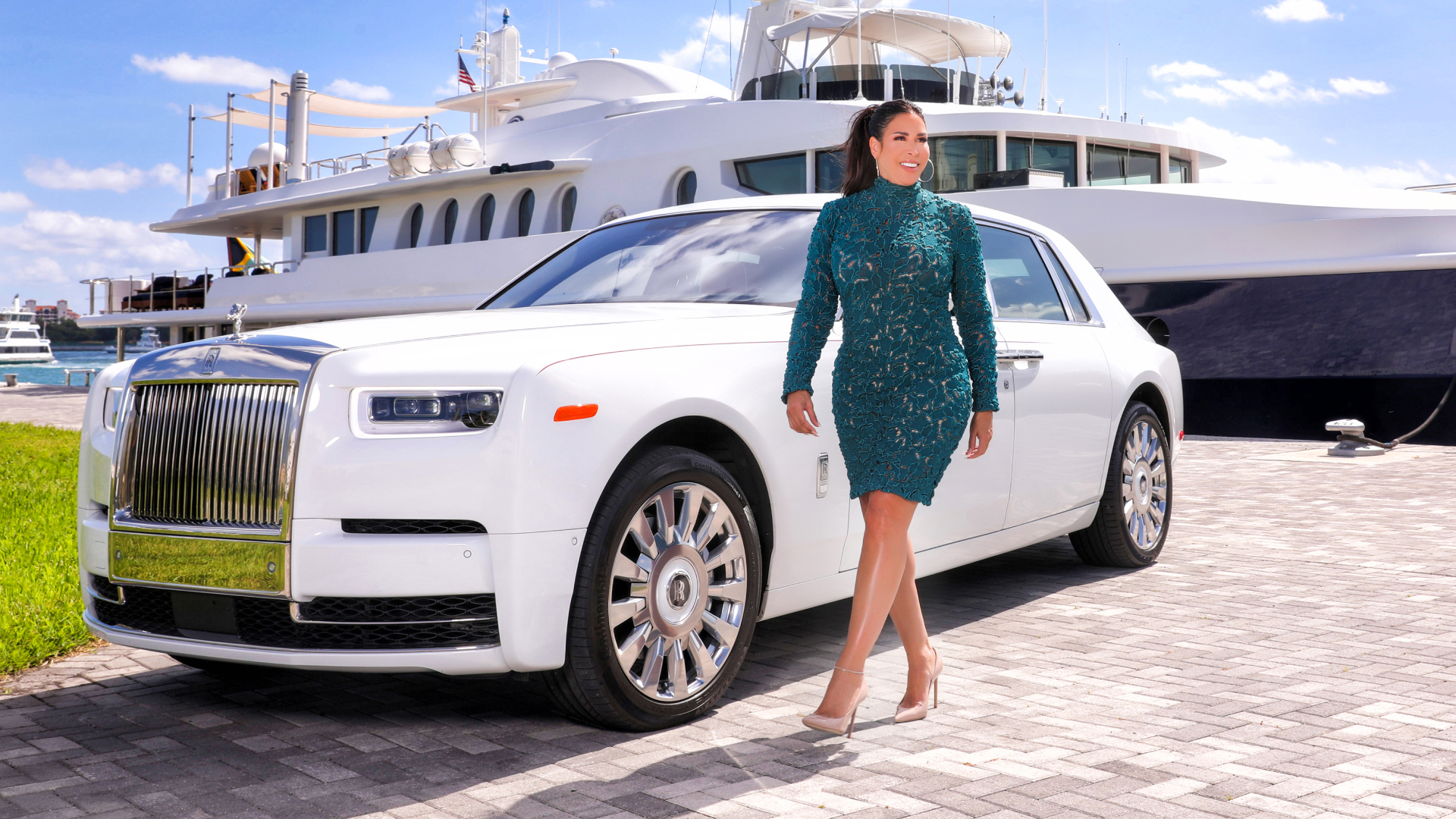 A photo of Carolyn Aronson wearing a green dress next to her Rolls-Royce and a boat