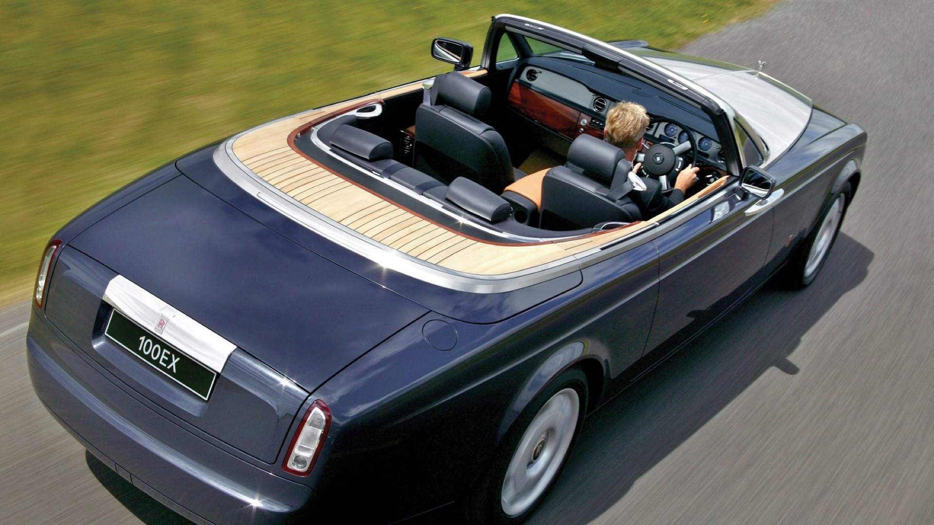 A drop-top Rolls-Royce motor car being driven along an open road.