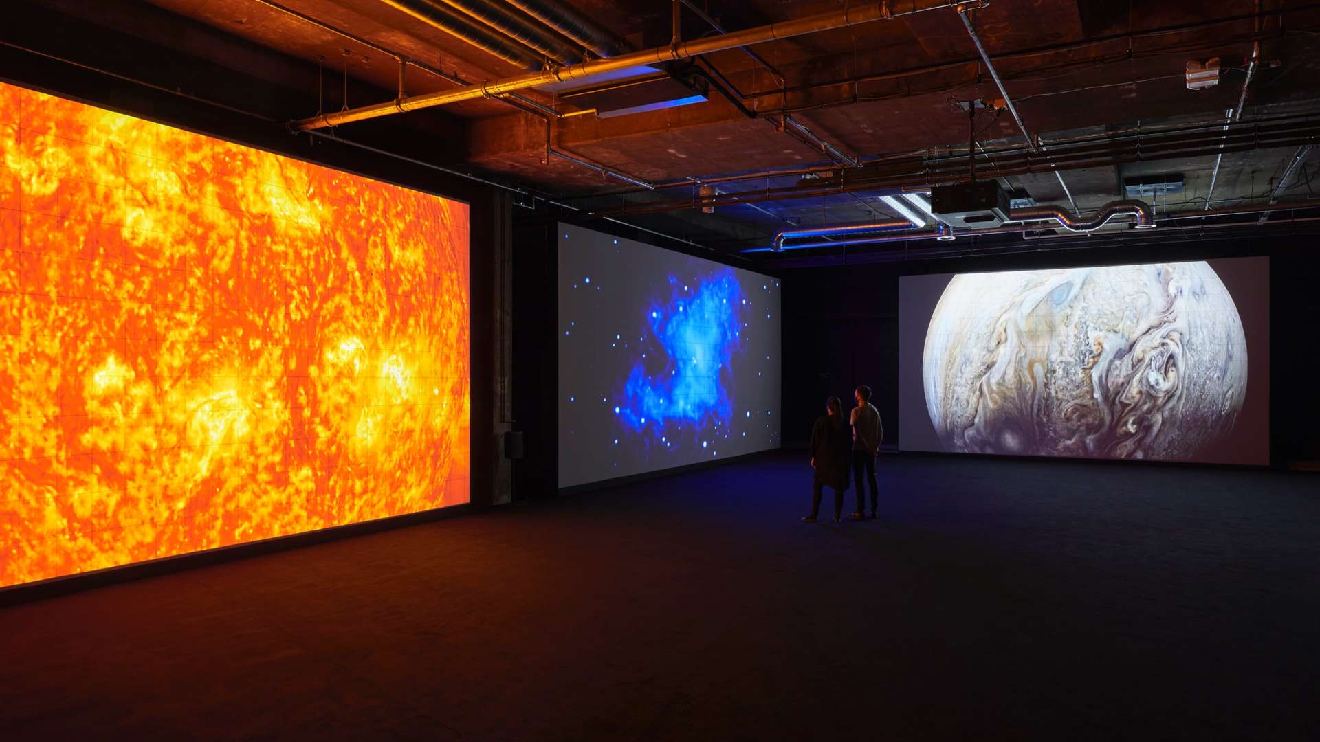 Two people stand inside exhibition space showing large-scale artwork by Japanese visual artist Ryoji Ikeda including images of outer space
