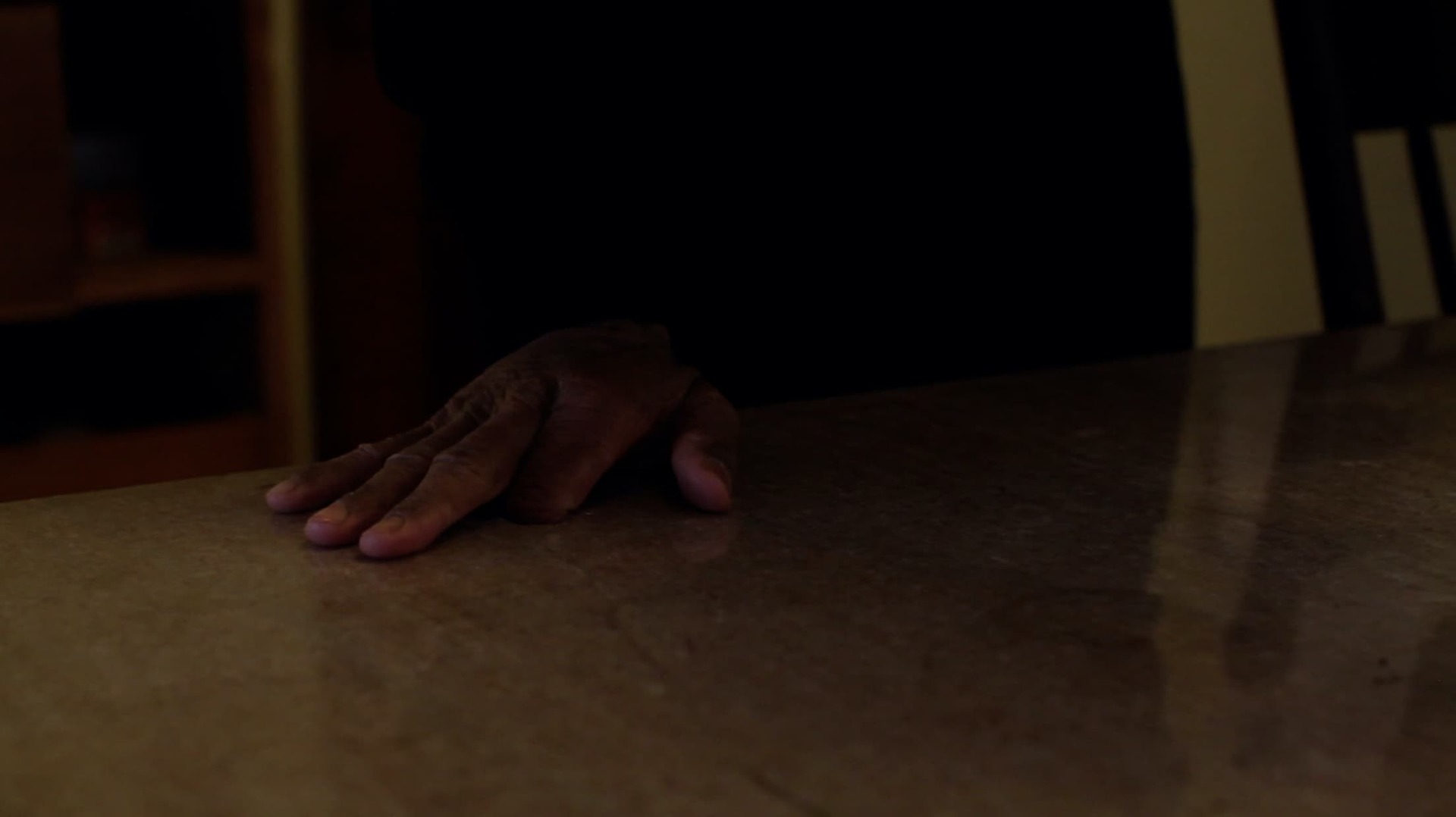 Still from 'Safehouse' - shows a hand, missing its pointer finger, resting on a wooden table