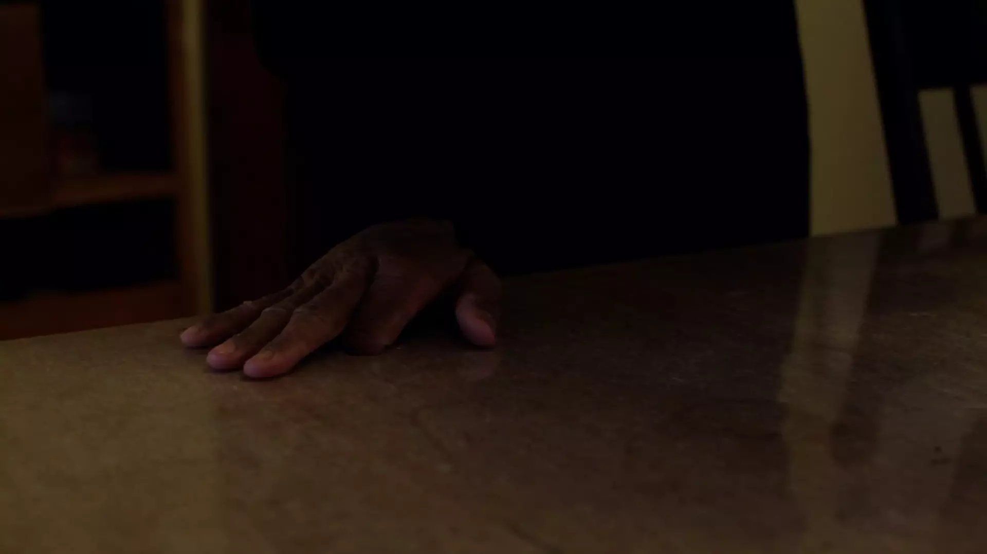 Still from 'Safehouse' - shows a hand, missing its pointer finger, resting on a wooden table