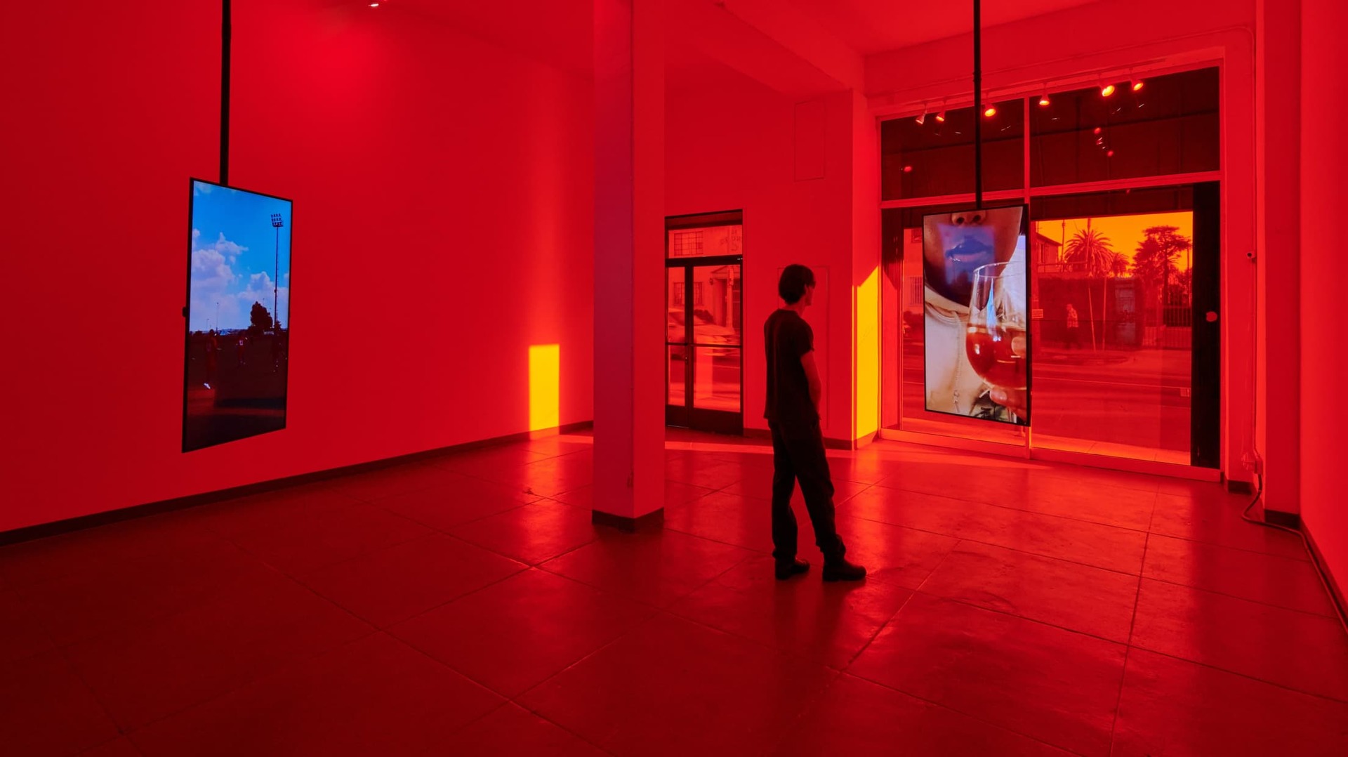 A shot of the installation 'Ugly Plymouths' shows a woman looking monitors displaying art work in a room cast in red light
