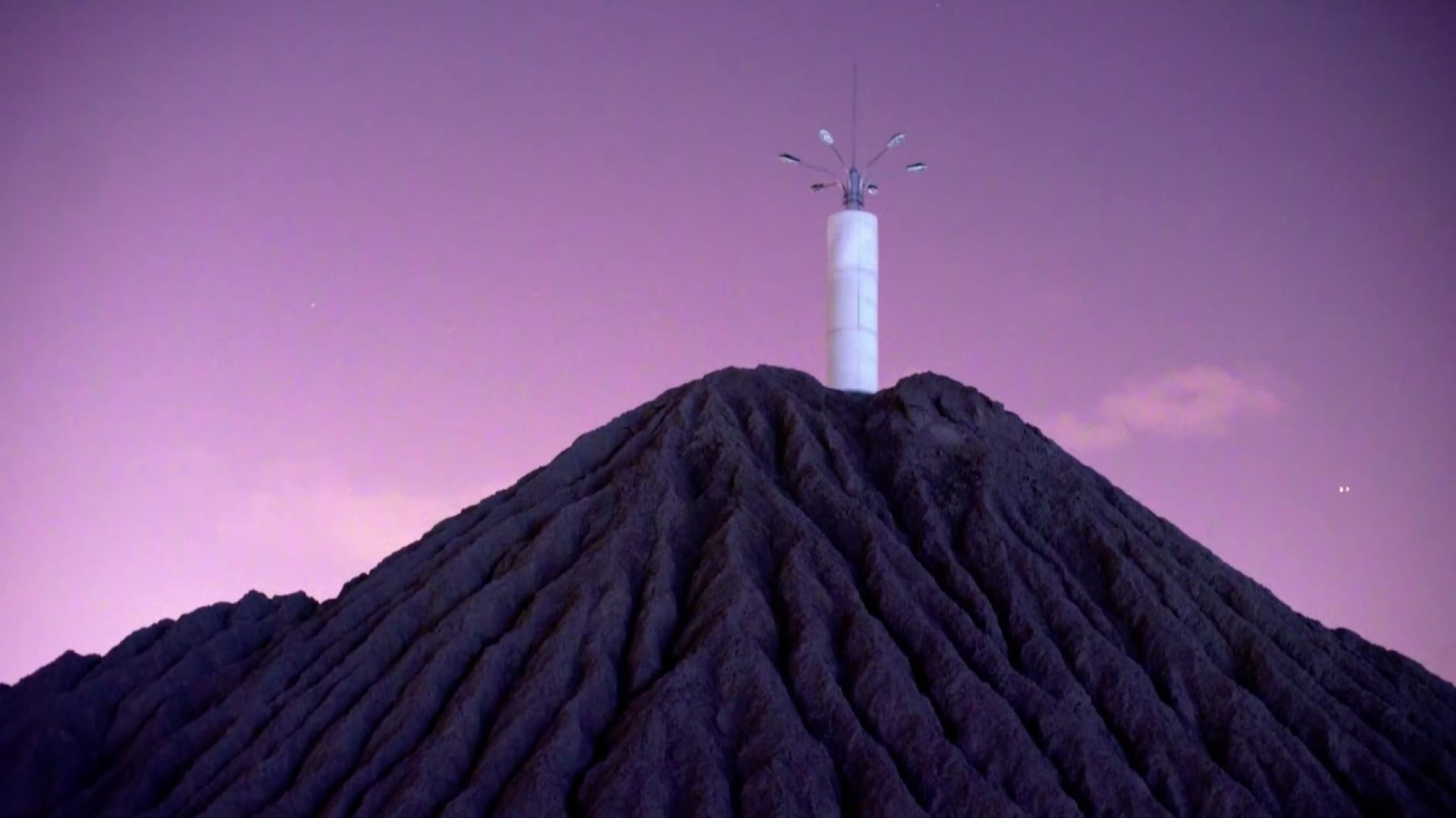 A still from Zhou Tao's Bienalle Arte 2017 entry, depicting a tower of lights against a purple hue night sky, atop a mountain