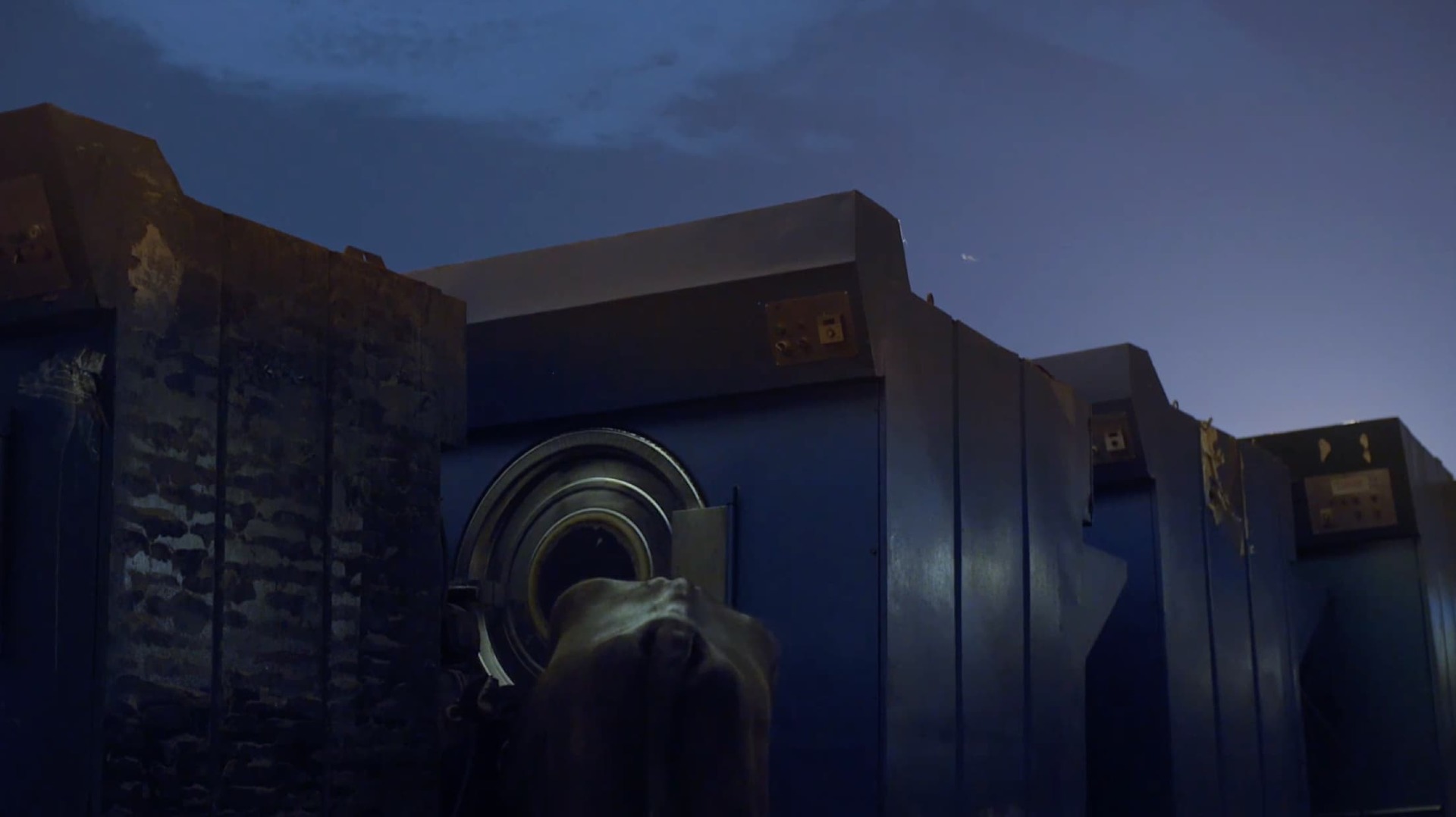 A still from 'The Worldy Cave' trailer depicting a dark blue night scene with machinery 