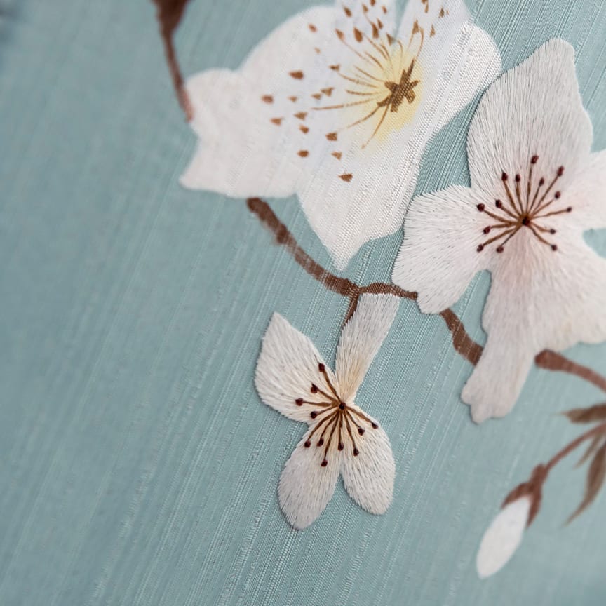 Discover the artistry of an icon enveloped in fine Chinese silk and embroidered with a hand-painted blossom motif.