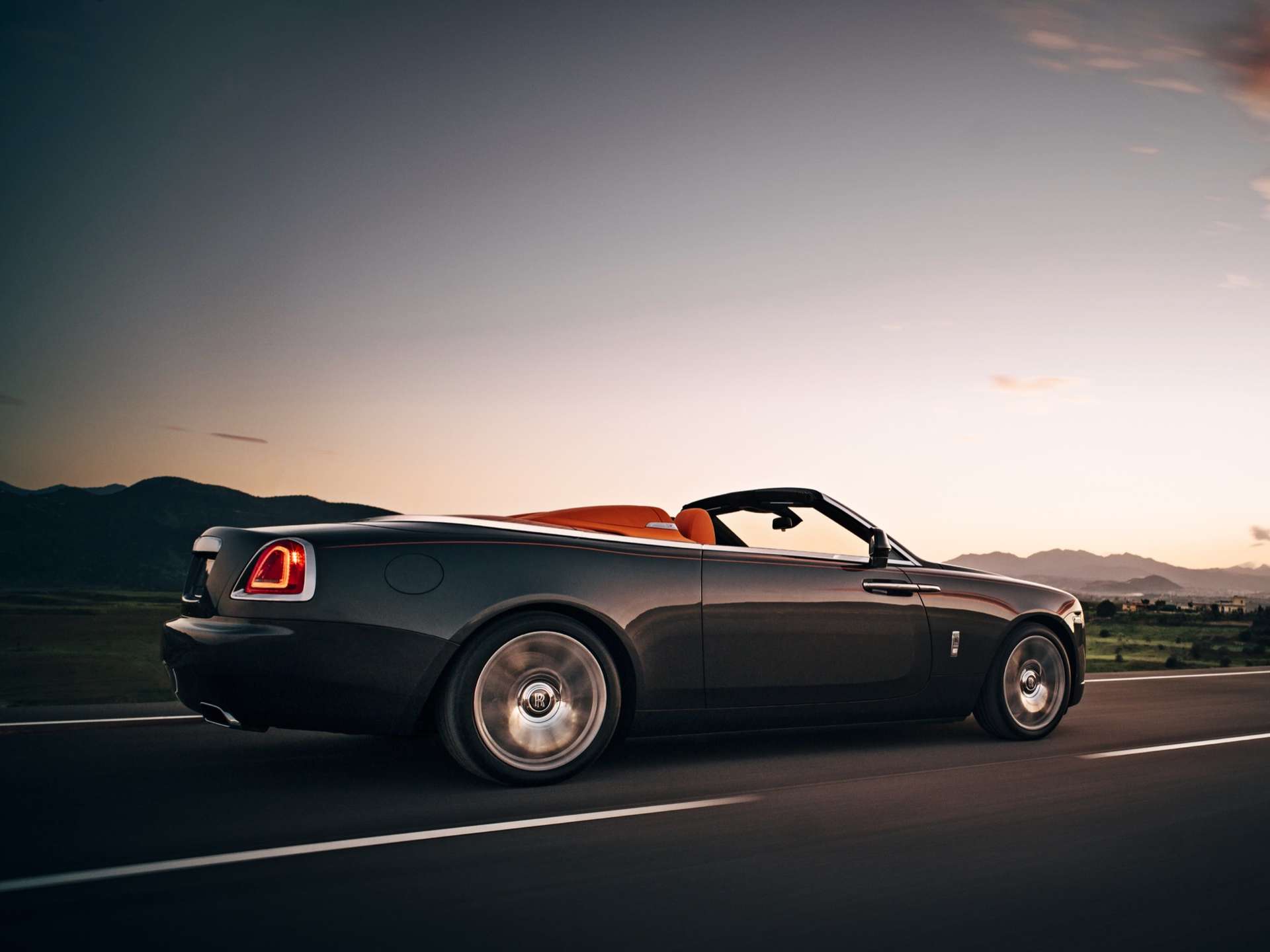 A grey Rolls-Royce Dawn motor car seen driving down an empty road.
