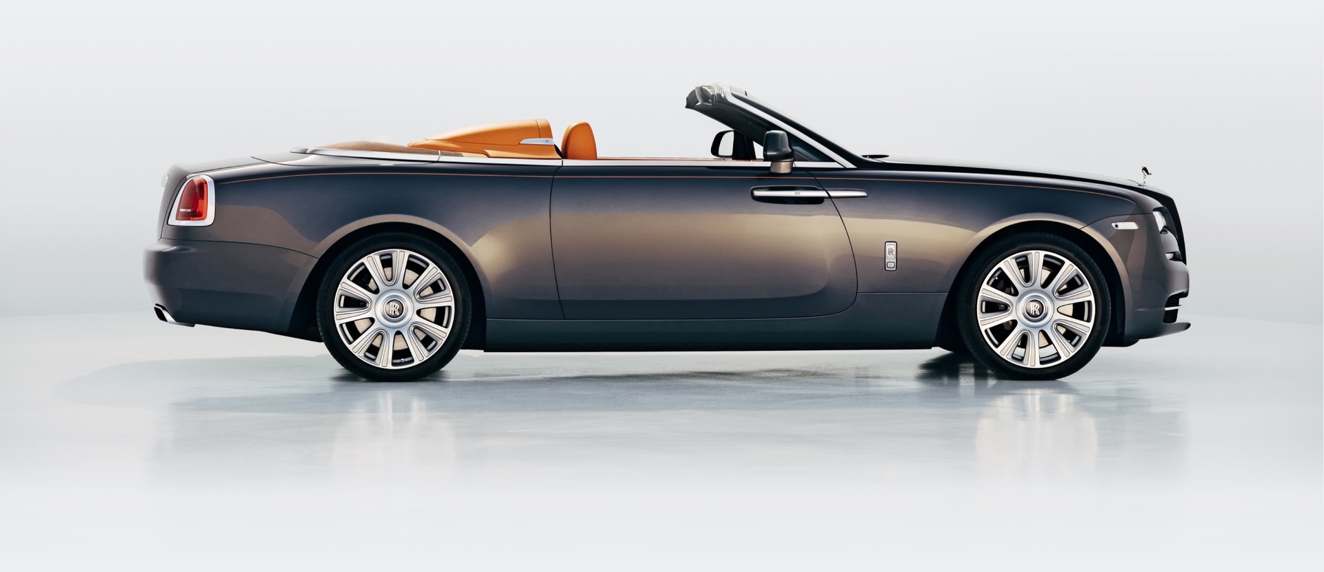 A side on angle of a grey Rolls-Royce Dawn with its roof down.