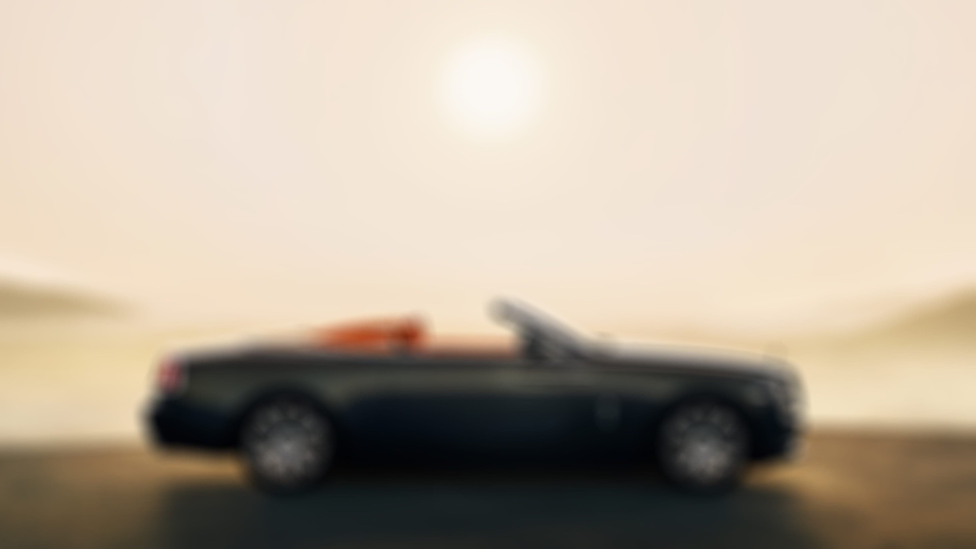 Side exterior view of a stationary Rolls-Royce Dawn Aero Cowling motor car with the tonneau cover roof down in sunny landscape