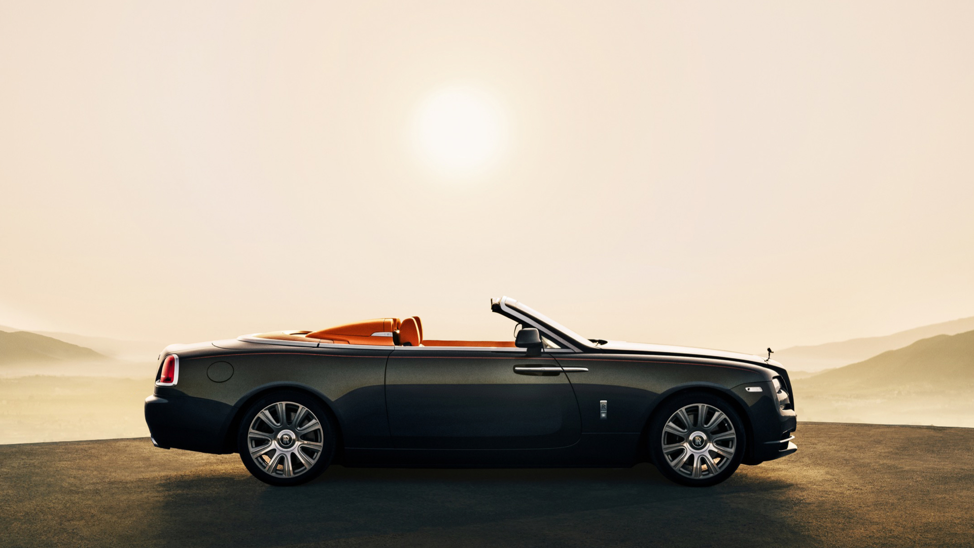 Side exterior view of a stationary Rolls-Royce Dawn Aero Cowling motor car with the tonneau cover roof down in sunny landscape