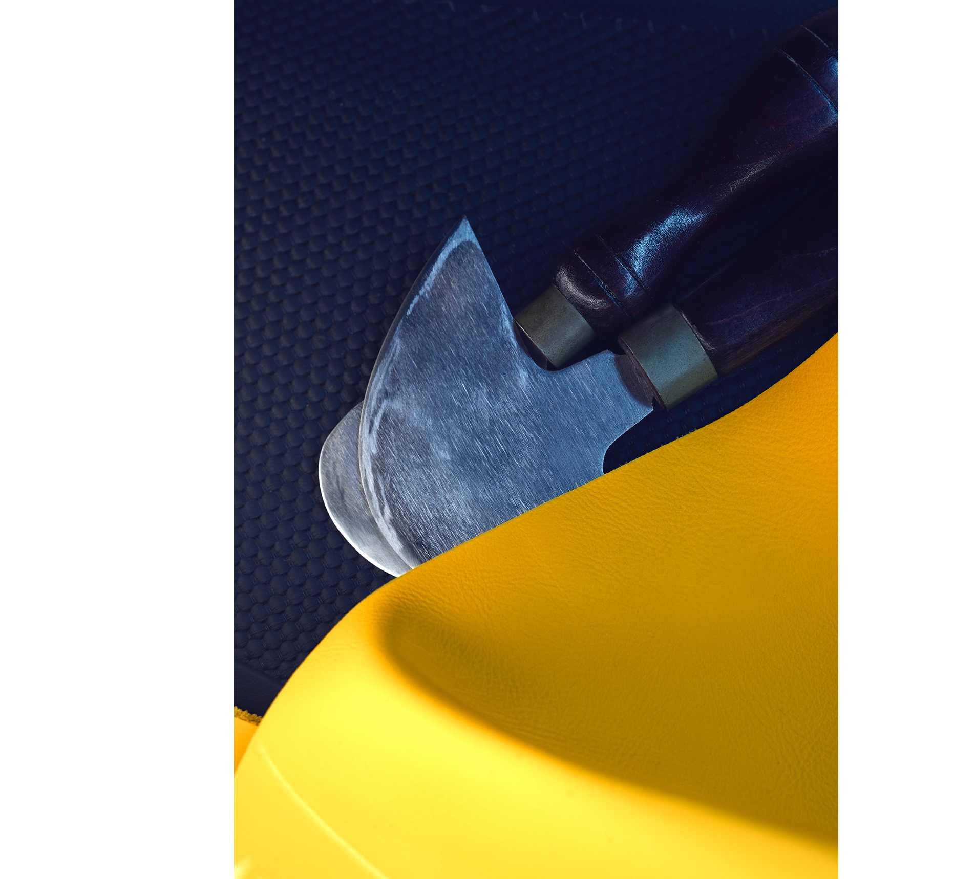 A close up shot of two sheets of leather, one blue and the other yellow, alongside a pair of leatherworking tools