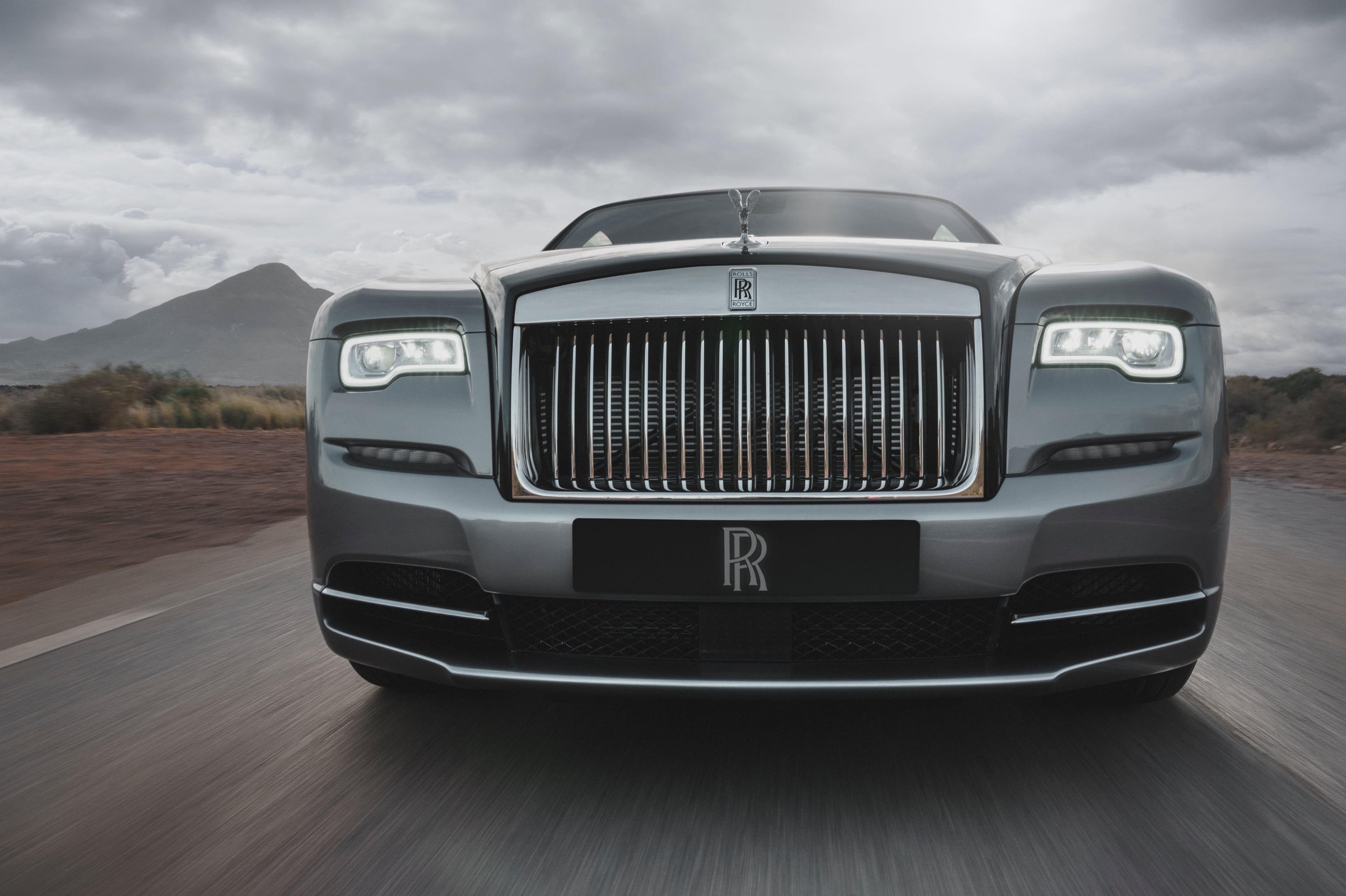 路上のロールス・ロイスWRAITH、フロントのライトとグリルをクローズアップした左右対称の構図、山々を背景に