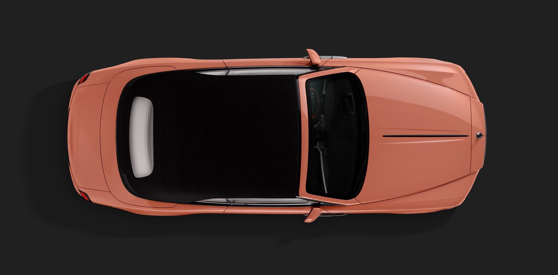 Фото с высоты птичьего полета: автомобиль Rolls-Royce Black Badge Dawn кораллового цвета, представленный на Pebble Beach, с поднятой крышей.