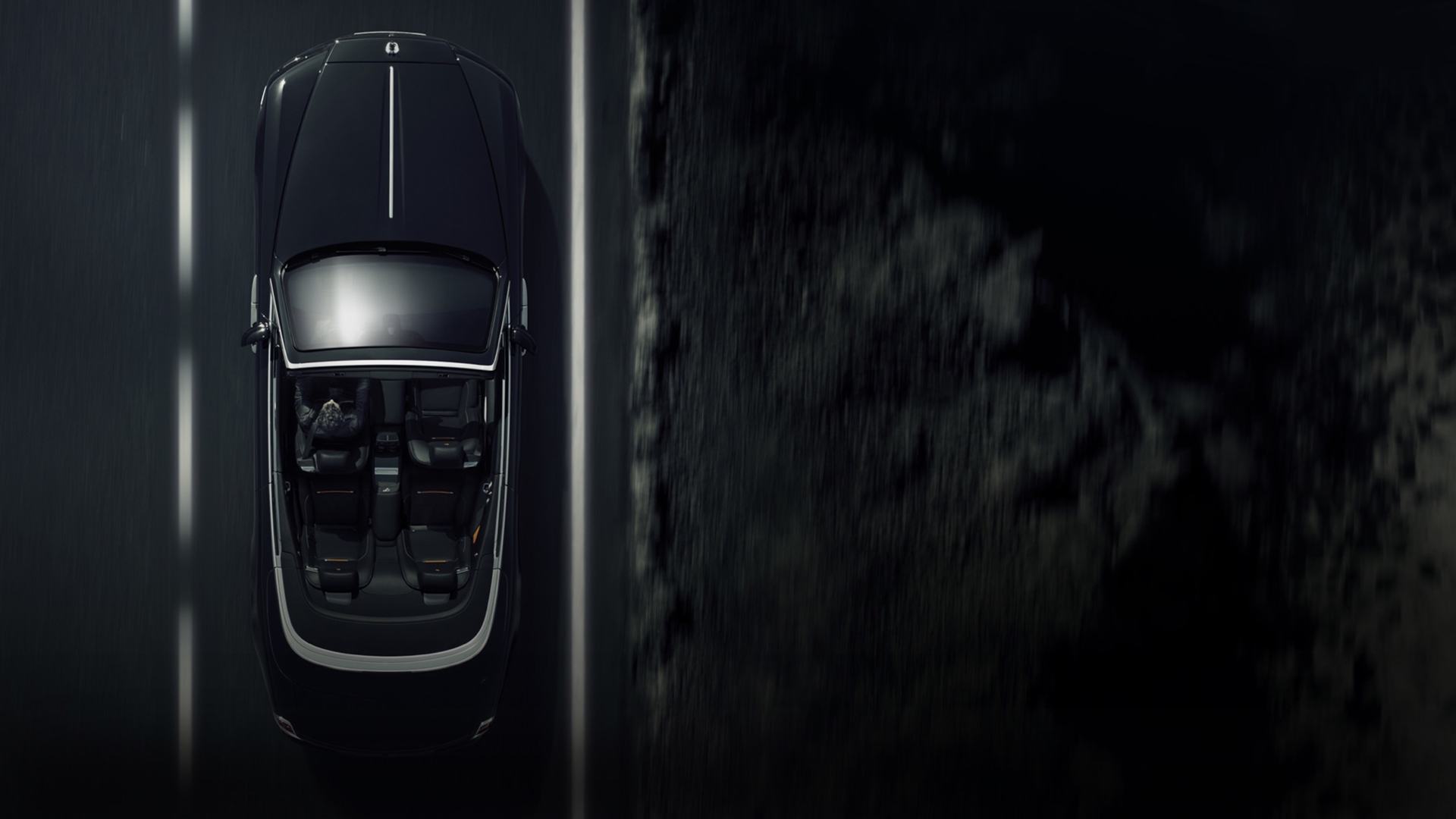 An aerial view of a Rolls-Royce Black Badge Dawn in motion on the road with the roof down.