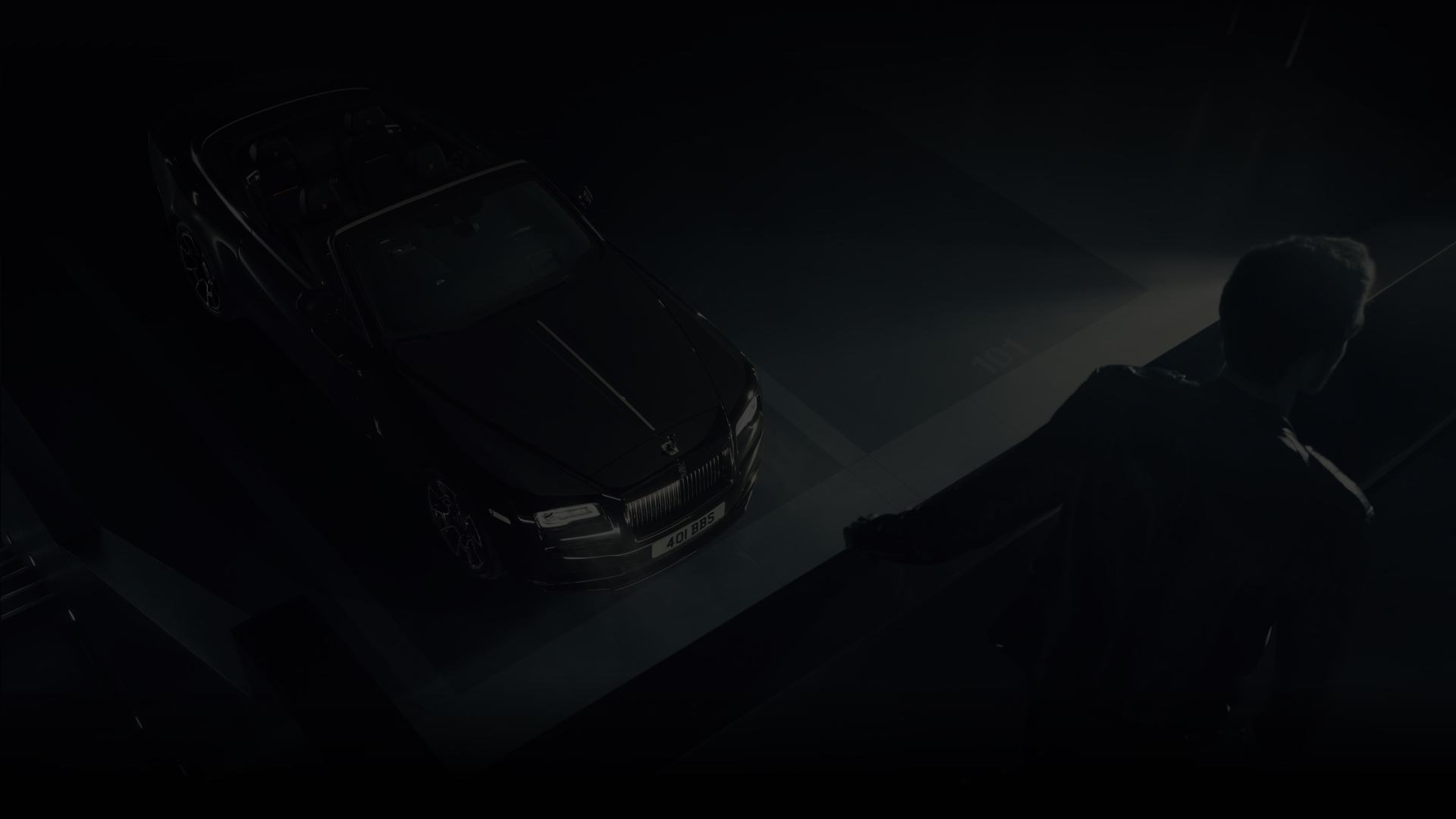 A shot of Rolls-Royce Black Badge Dawn parked in a driveway, while a gentleman stands on a balcony above.