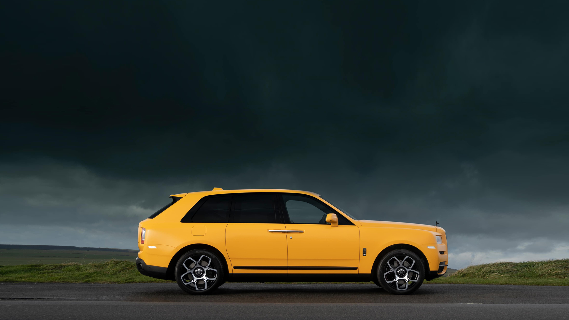 Side exterior view of the Rolls-Royce Black Badge Cullinan Capella motor car stationary with grey clouds above