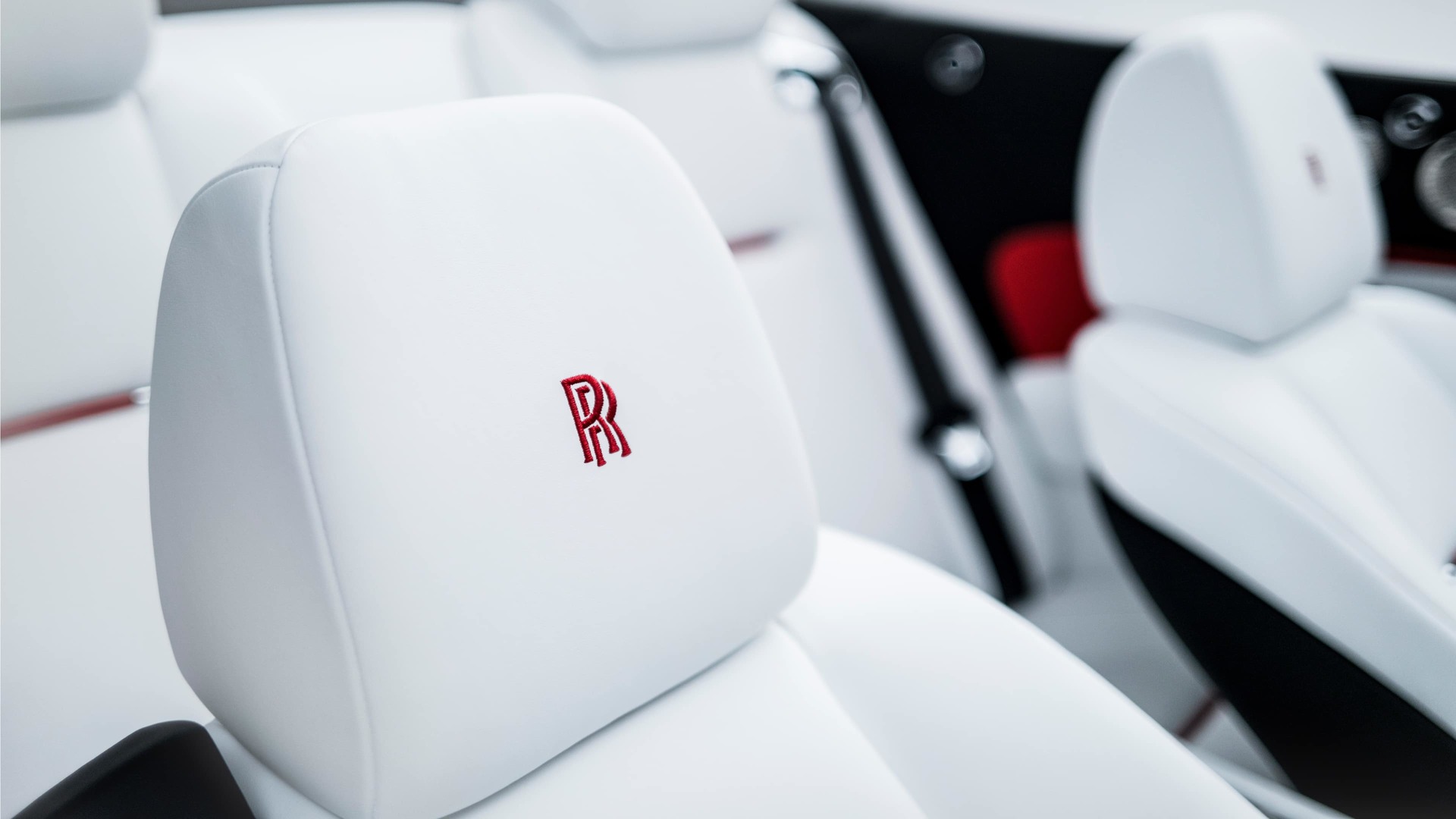 Signature Rolls-Royce monogram in Koi Red embroidered onto white leather headrests of a Rolls-Royce motor car 