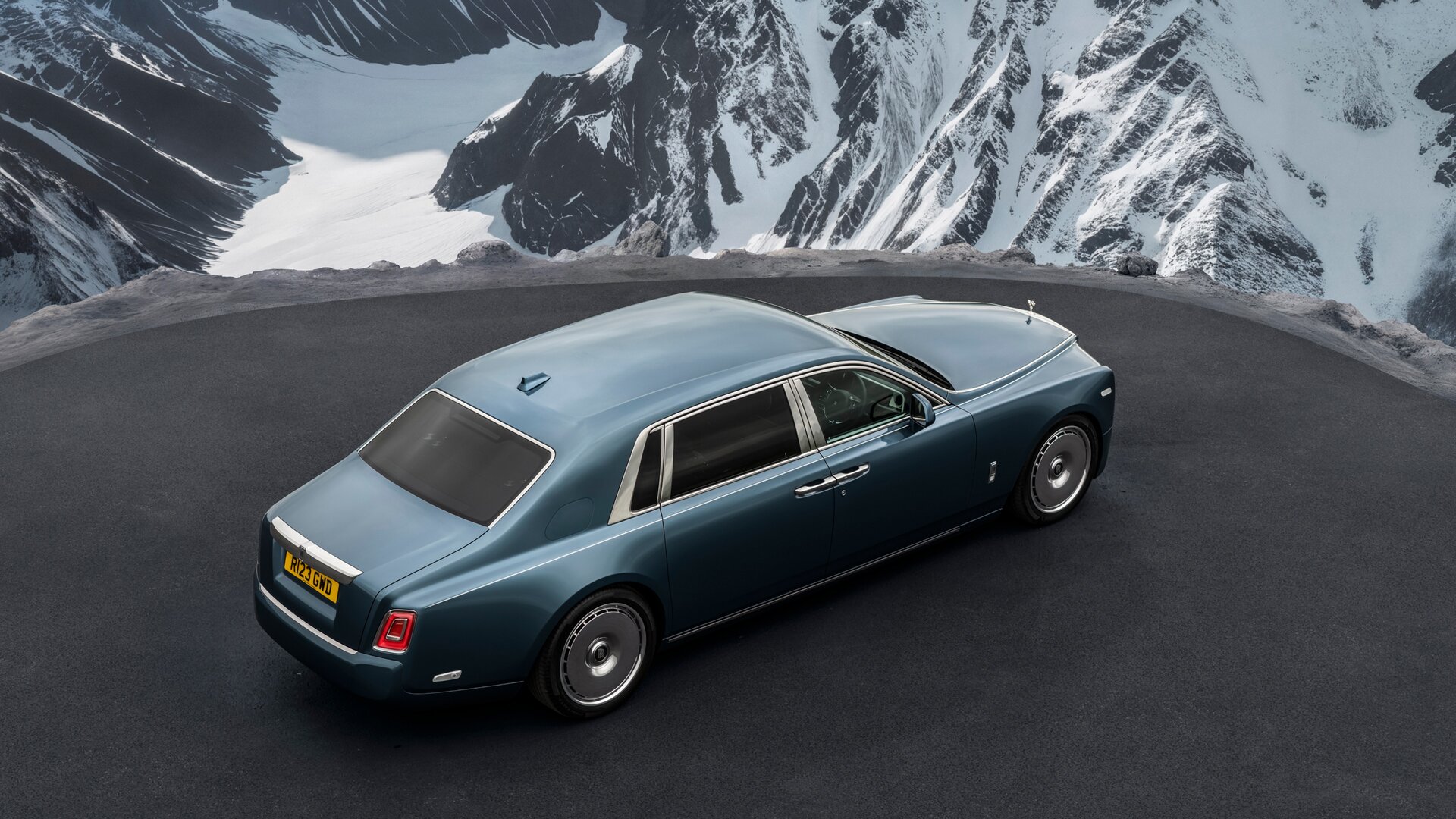 overhead of a blue Phantom extended parked on a mountain road overlooking a snowy mountain landscape