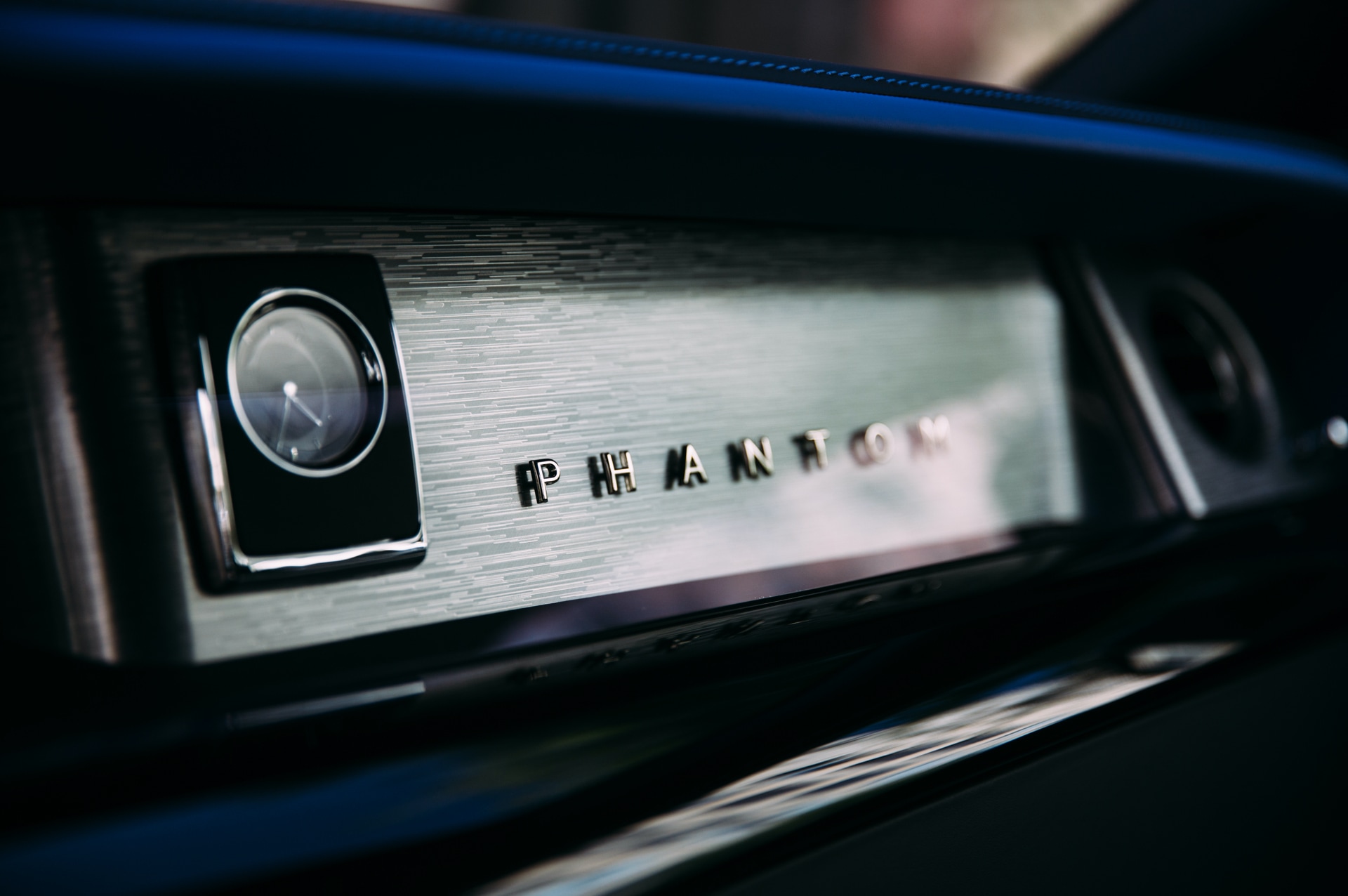 A close up shot of the dashboard of a Rolls-Royce Phantom, showing the wood grain and embossed layered lettering spelling Phantom