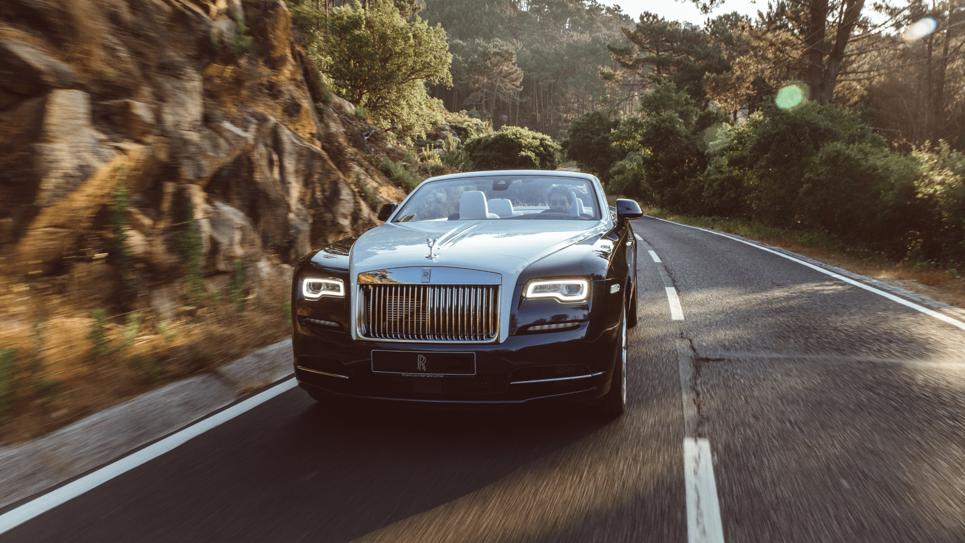 A blue and silver Rolls-Royce Dawn on the road with the top down