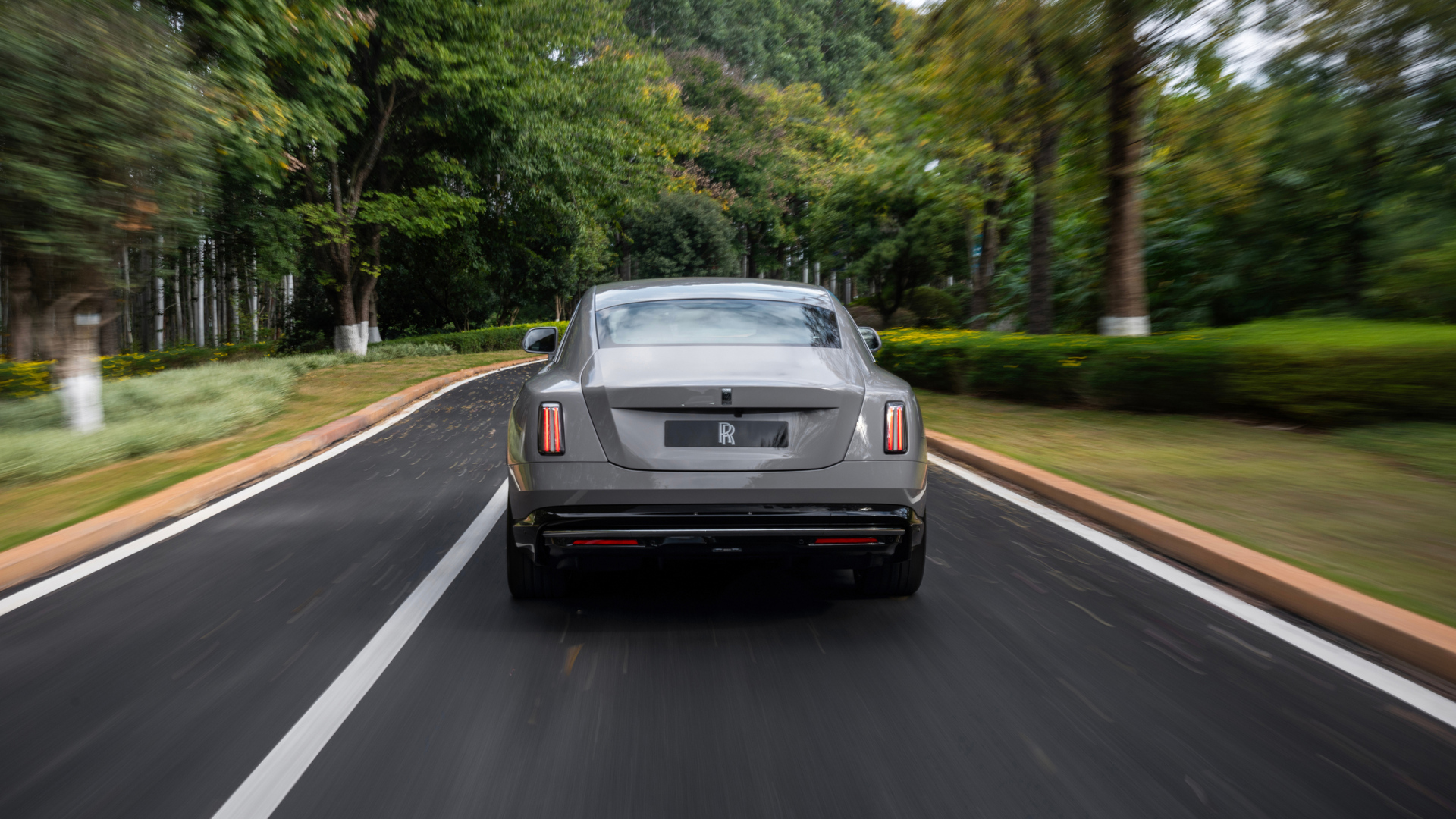 Back angled shot image of a grey Spectre driving through a winding street.