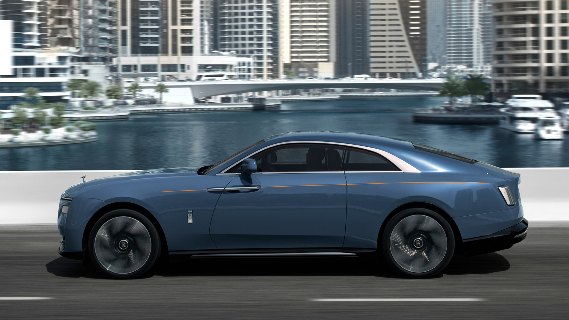 Horizontal shot of the Spectre driving over a bridge with skyscrapers in the background.