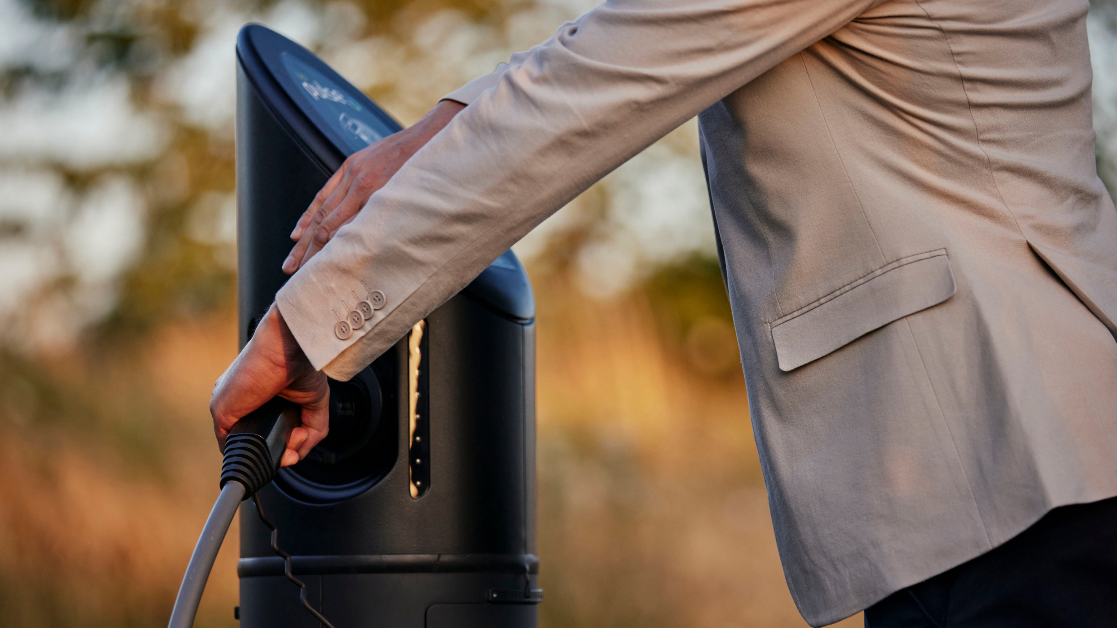 A man pulling the the charging cable out of a public charging station to charge his Spectre